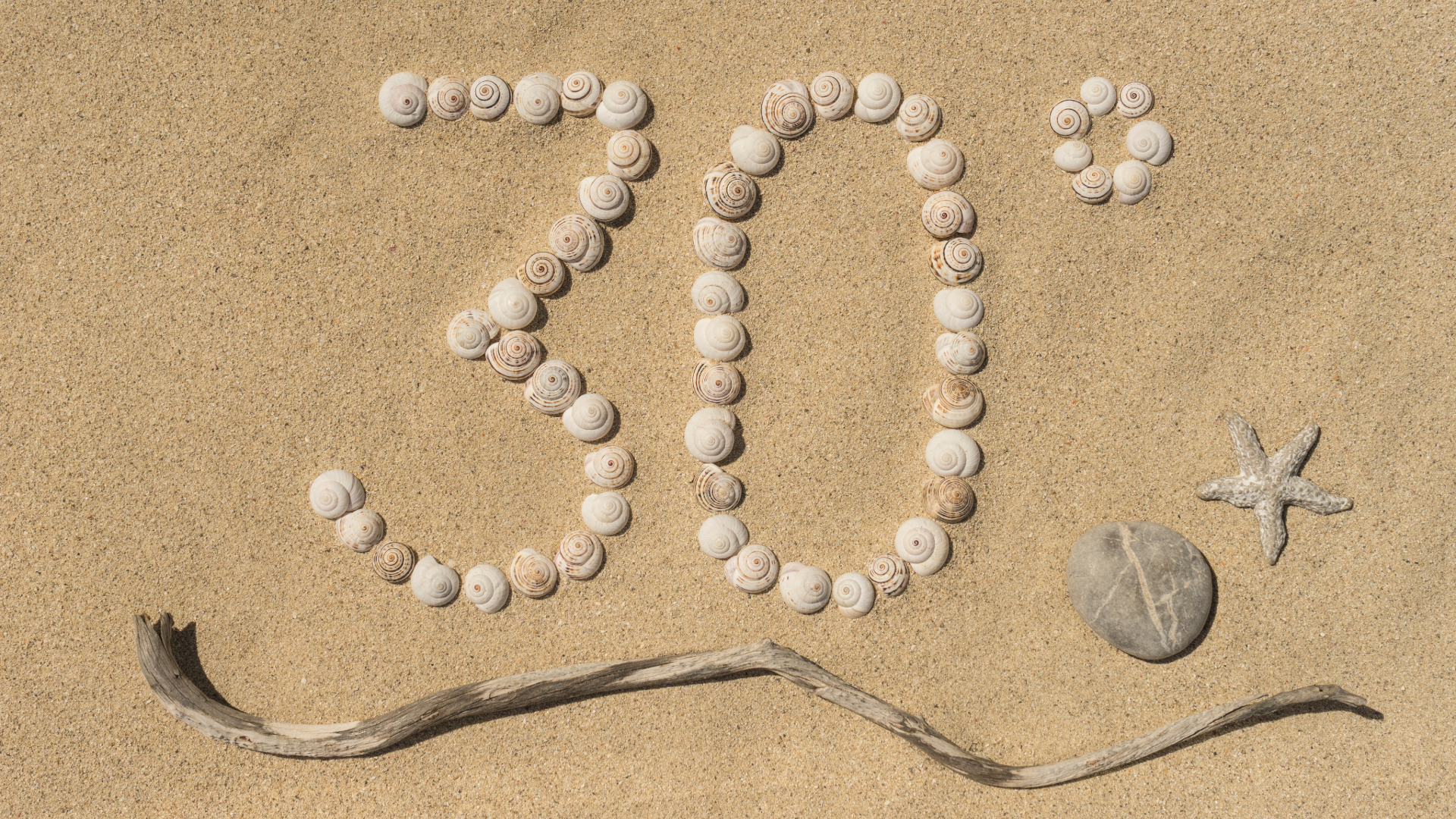 Le chiffre 30° est formé par des coquillages sur du sable, un bâton de bois flotté en dessous et une carte de valeur estivale à droite d’une pierre et d’une étoile de mer.