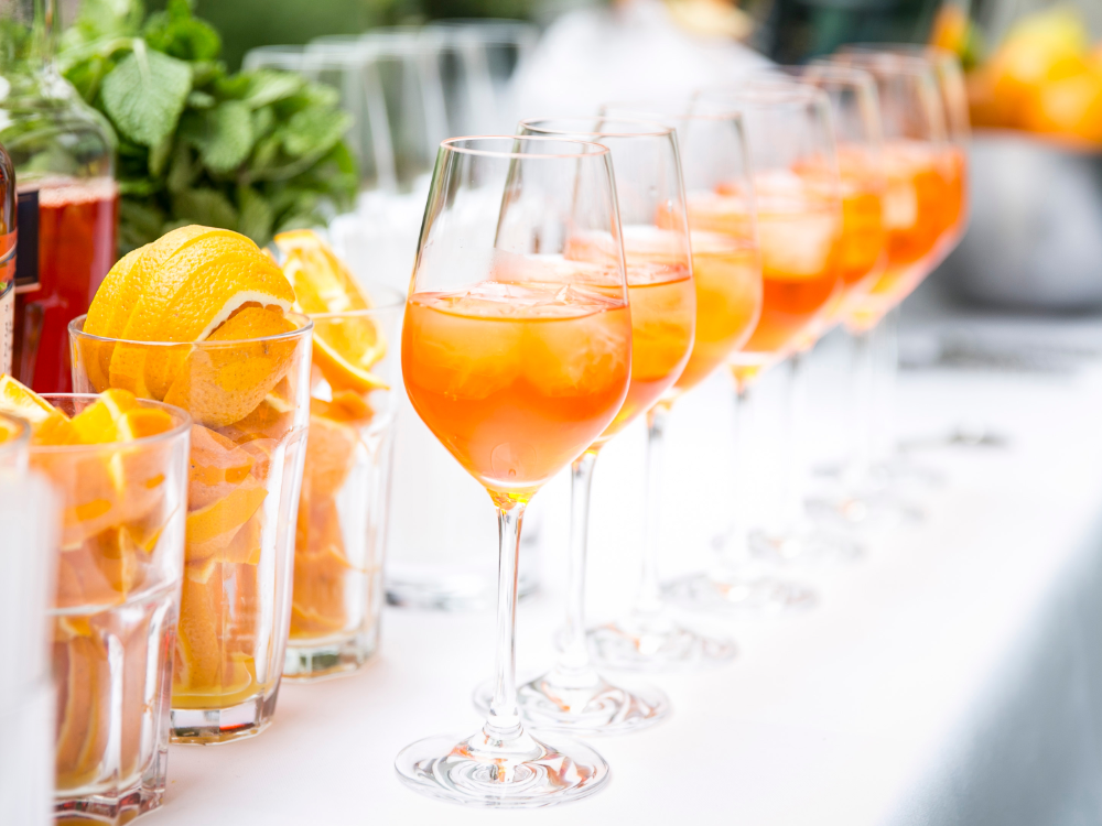 Sur une table se trouvent plusieurs verres à vin remplis de cocktails à l’orange et de glace, ainsi que des verres avec des tranches d’orange et de la menthe fraîche – parfaits pour profiter de la carte prépayée d’été par un après-midi ensoleillé.