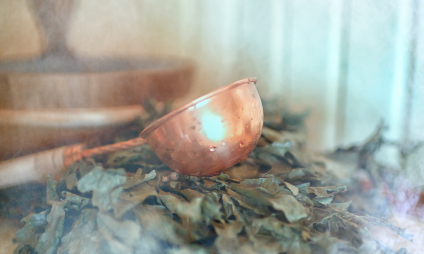 Une truelle cuivrée repose sur un paquet de feuilles sèches. La vapeur ou la brume tourbillonnent autour et créent une atmosphère douce et éthérée – parfaite pour un coup de pied frais et rafraîchissant selon Kneipp.